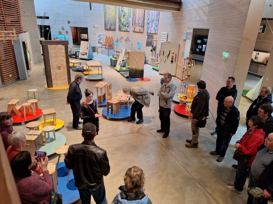 Näkymä puuseinäiseen tilaan. Sisätiloissa alakerrassa on useita erilaisia puusta tehtyjä esineitä, joita joukko ihmisiä katselee.
