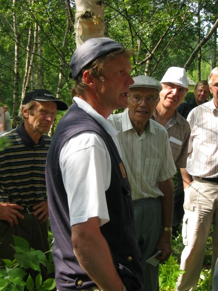 Miesryhmä seisoo koivikossa. Yksi miehistä puhuu ja toiset kuuntelevat. 